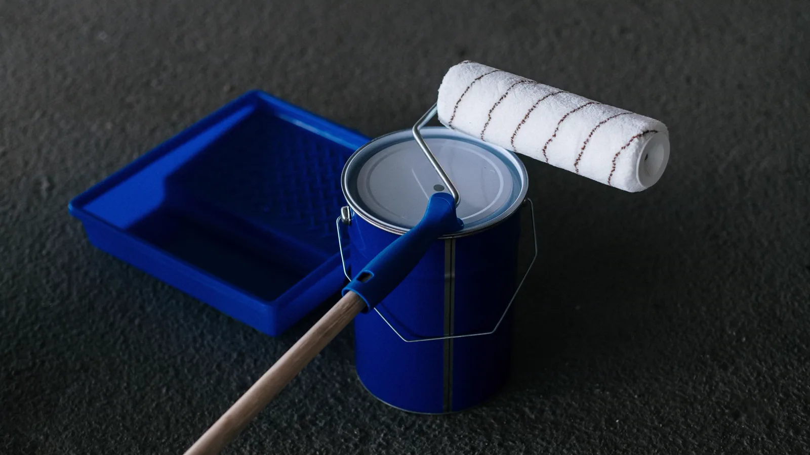 Paint roller resting on a paint can beside a blue tray