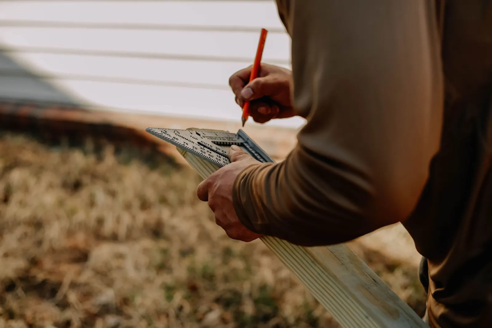 Hands marking a timber board with a square outdoors