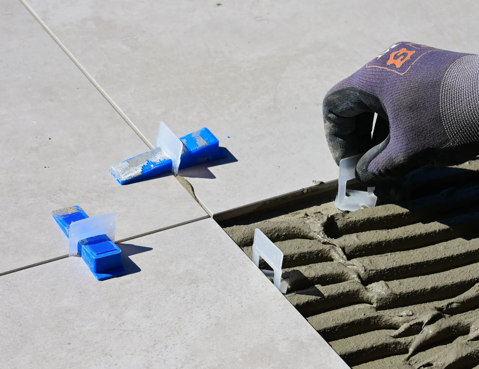 Hands setting large tiles with spacers and levelling clips