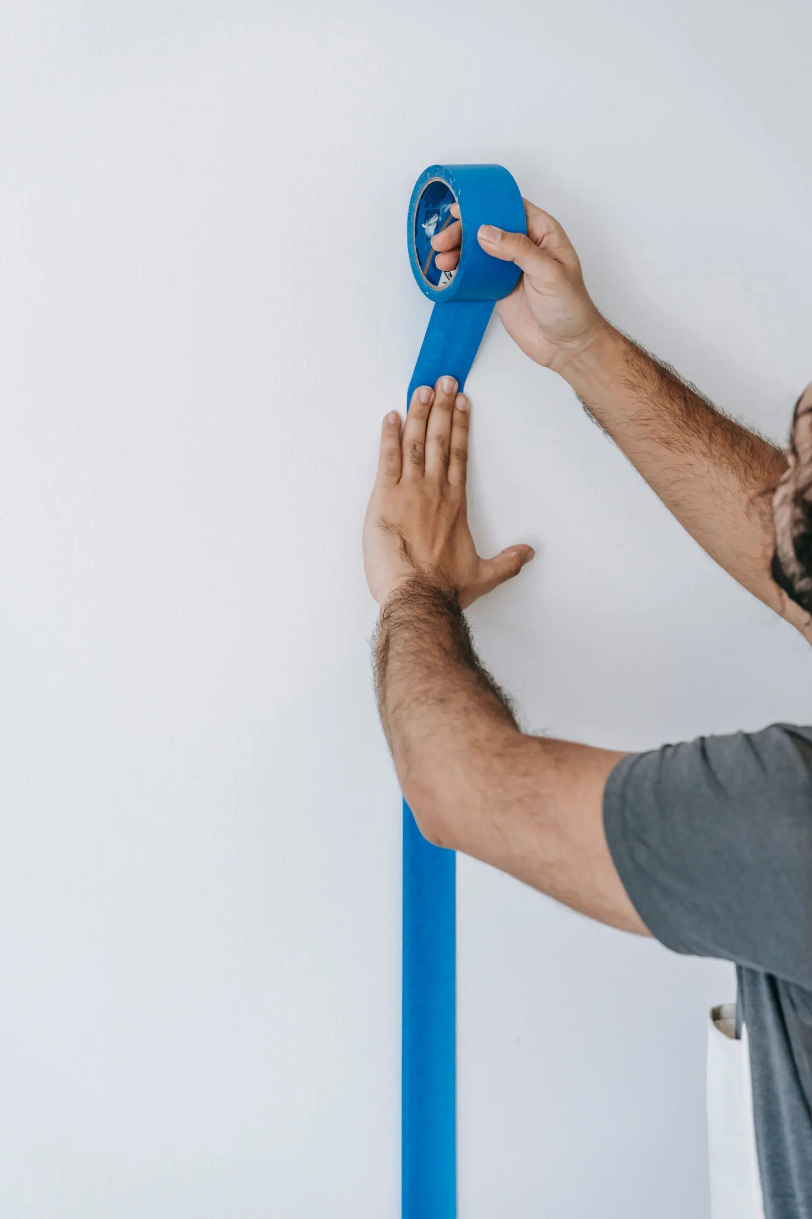 Hands pressing painter's tape along the edge of a wall