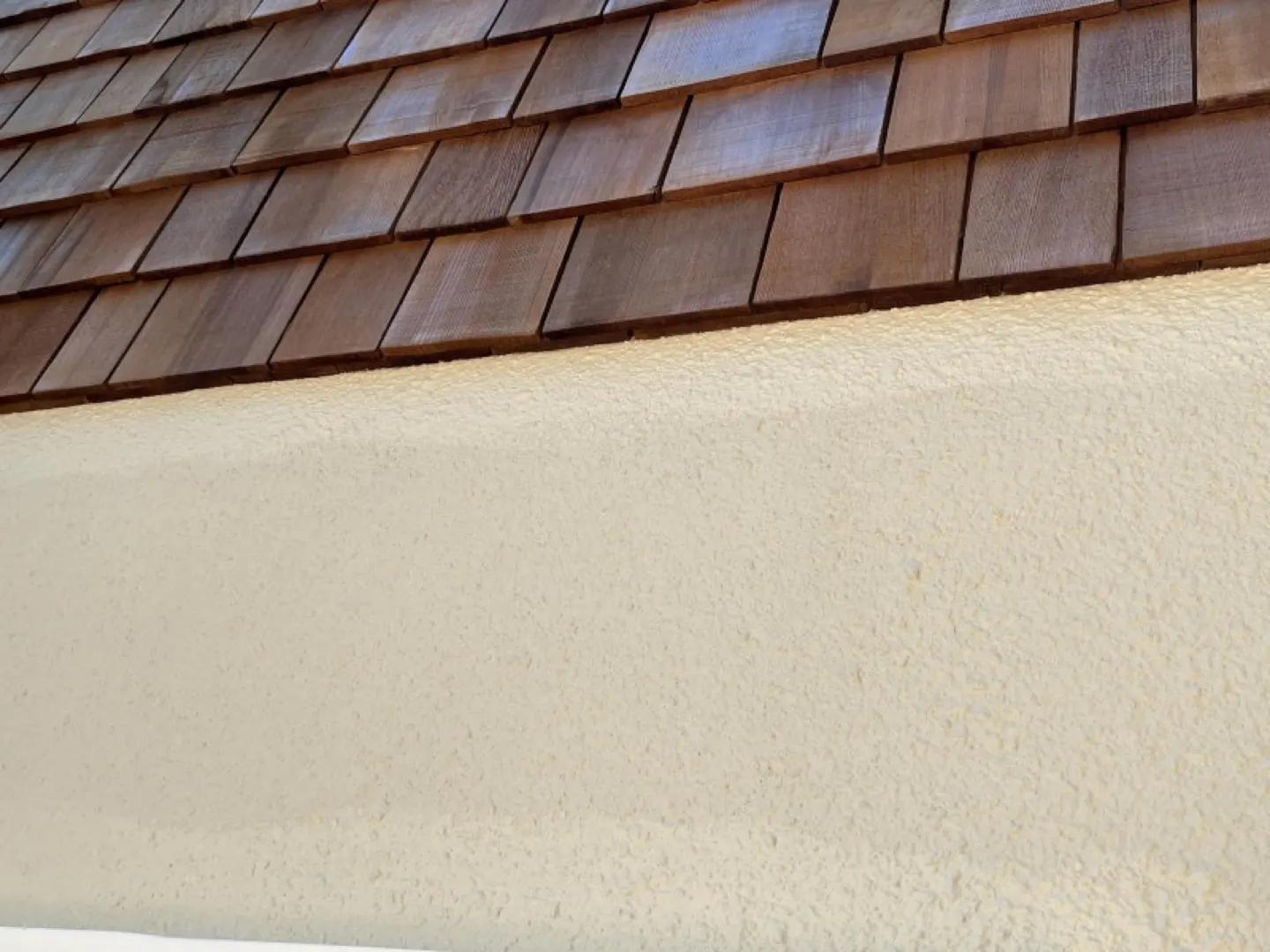Cedar shingle gable meeting a freshly painted cream plaster wall