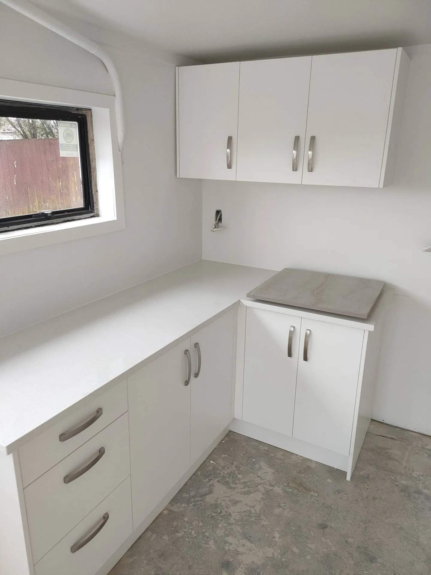 Finished white kitchen and laundry cabinetry with a stone-look benchtop leaning against the wall